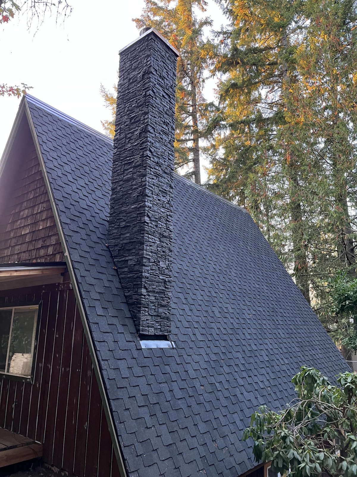 Steep A-frame roof in designer-cut shingles with stacked-stone chimney